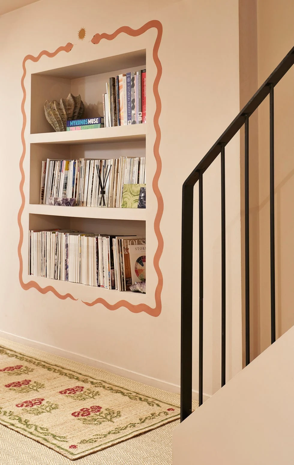 Recessed bookshelf with books and decor framed by wavy border next to stairs.
