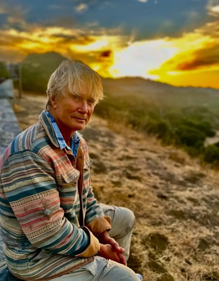 Richard Norton sitting outdoors with a sunset and hills in the background.