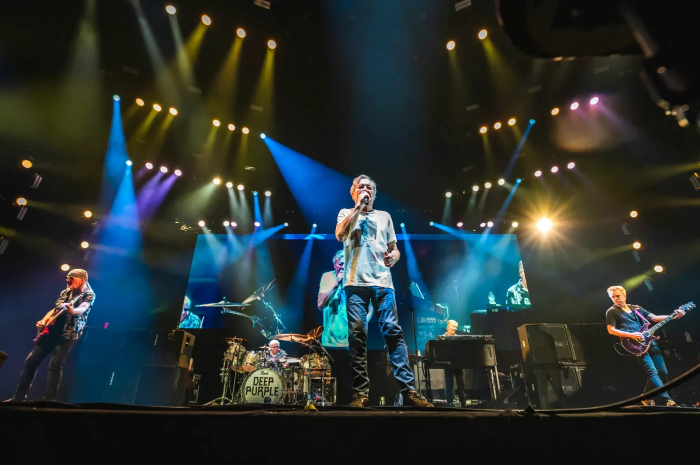 Rock band Deep Purple performs live on stage under dramatic blue and yellow stage lighting.