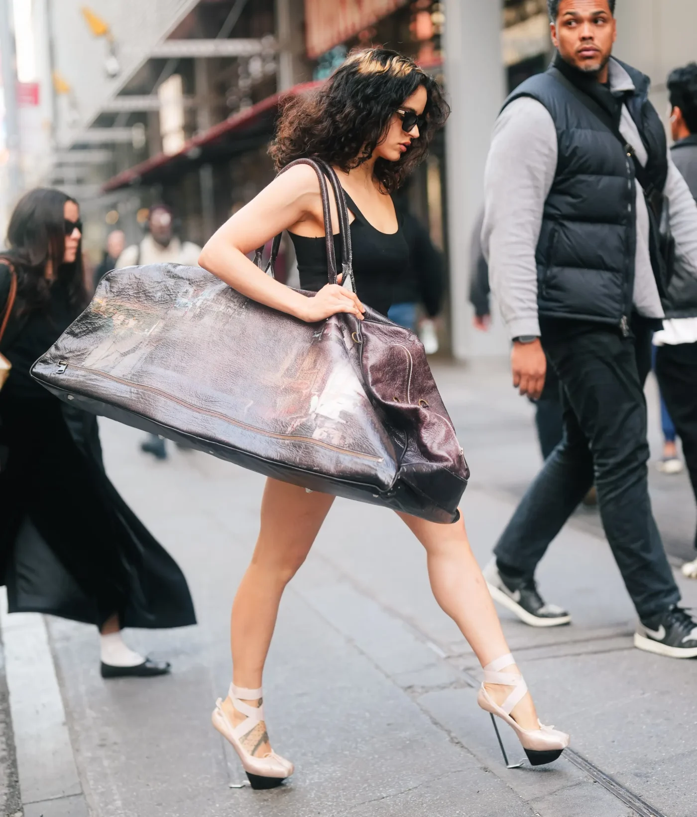 Rosalia walking down a New York City street carrying a large travel bag.