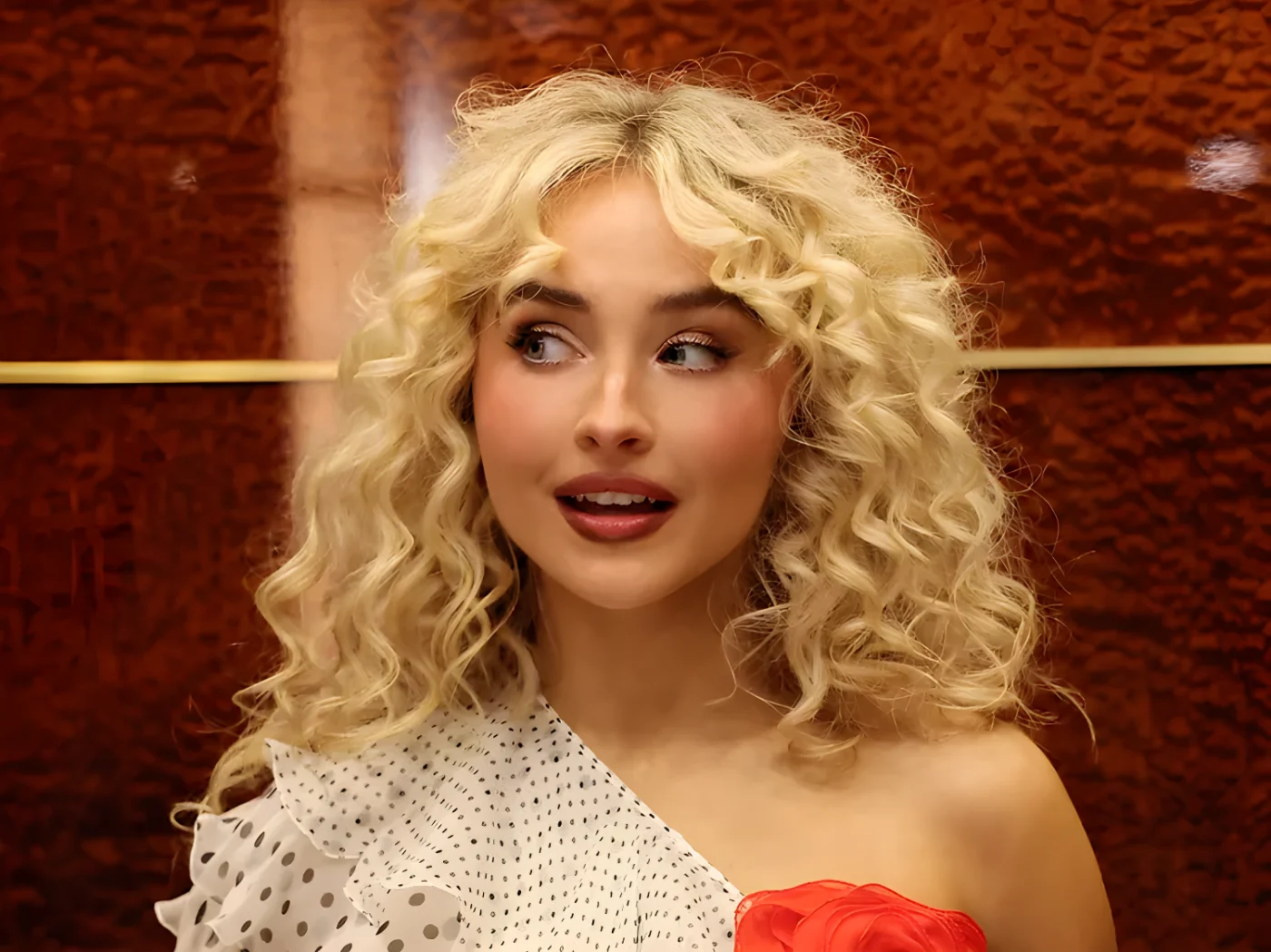Sabrina Carpenter looking to the side wearing a oneshoulder outfit with wavy hair