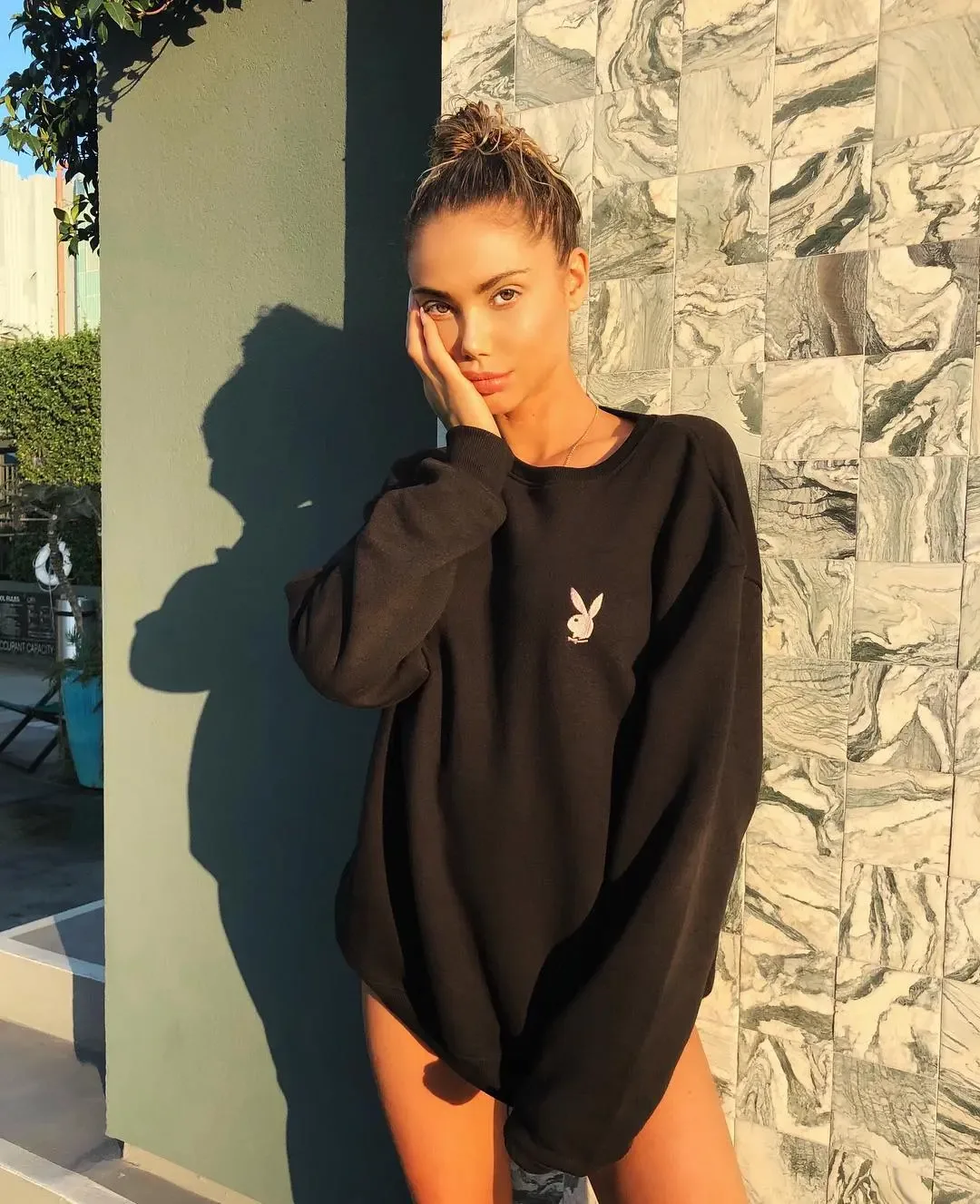 Sahara Ray in a black sweatshirt in front of a marble-tiled wall.