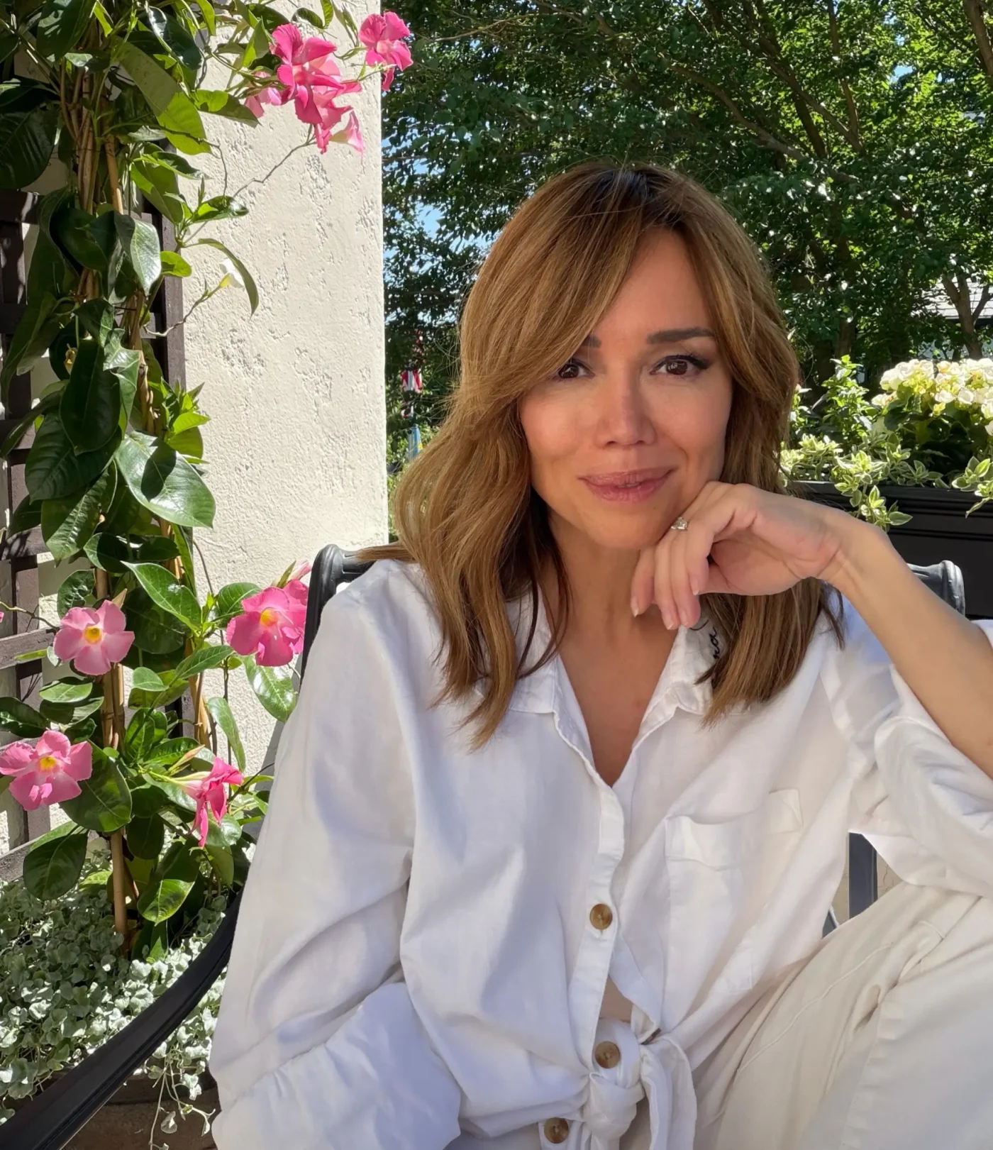 Sara Gore sitting outdoors with pink flowers and lush green plants in the background.