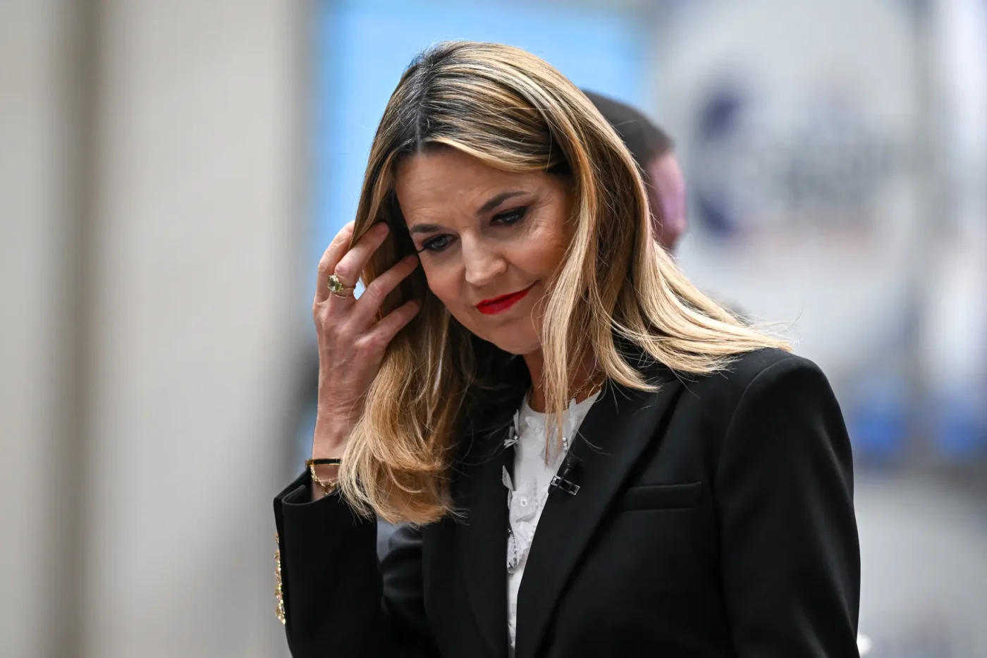 Savannah Guthrie adjusts her hair while wearing a black blazer.