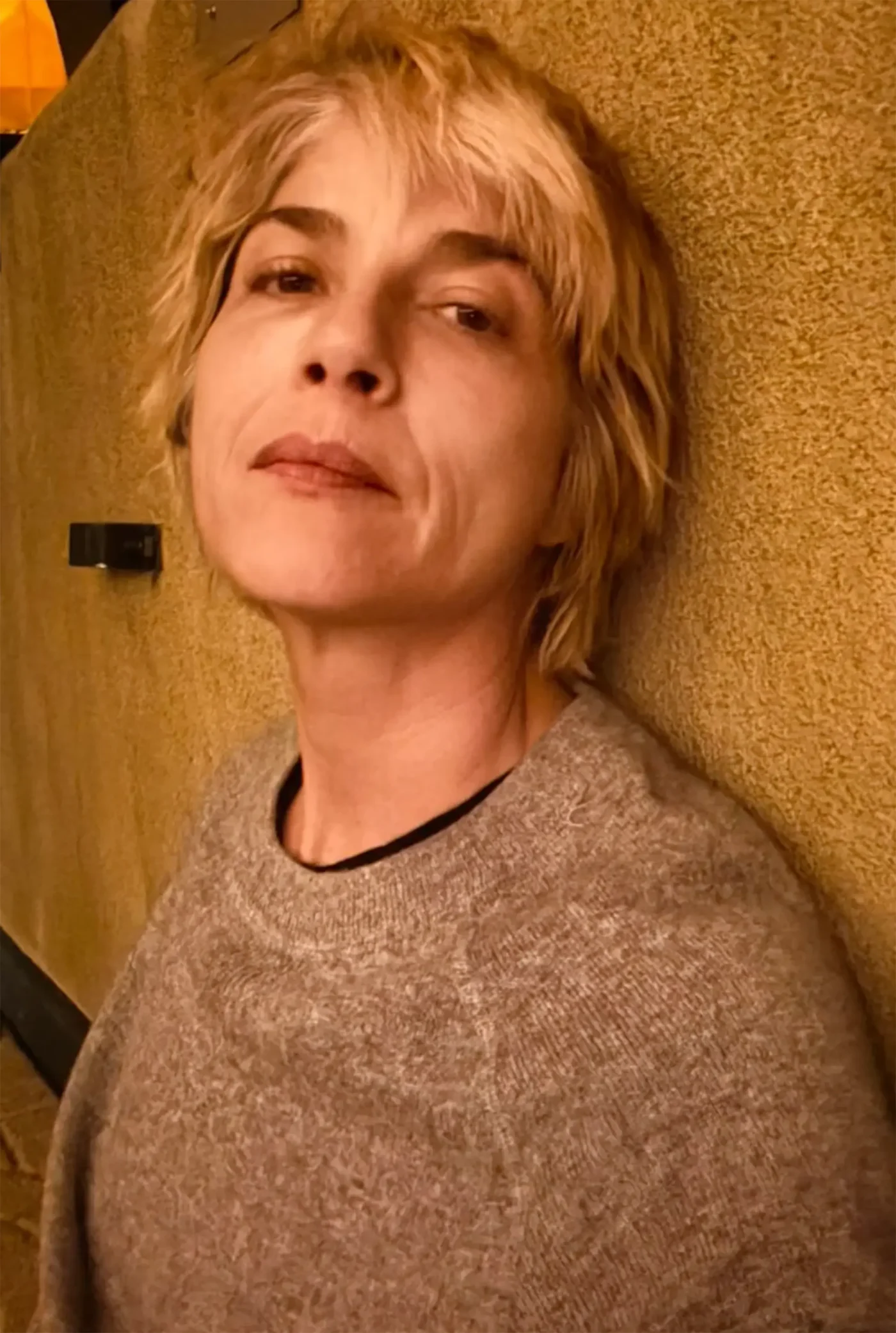Selma Blair leaning against a textured wall, wearing a grey sweater.