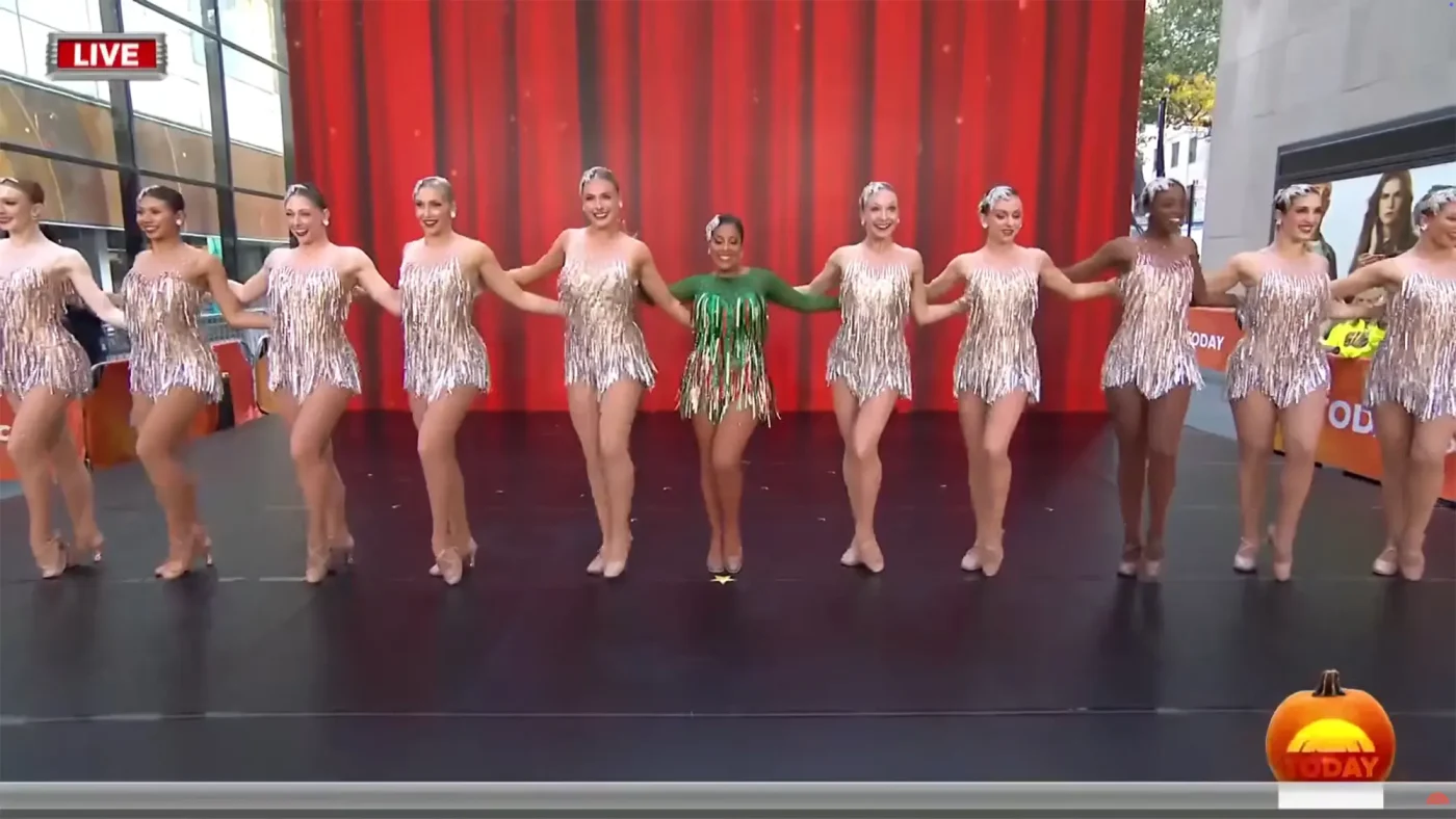 Sheinelle Jones, dressed in green, performs with a line of Rockettes in shimmering fringe dresses on the Today show.