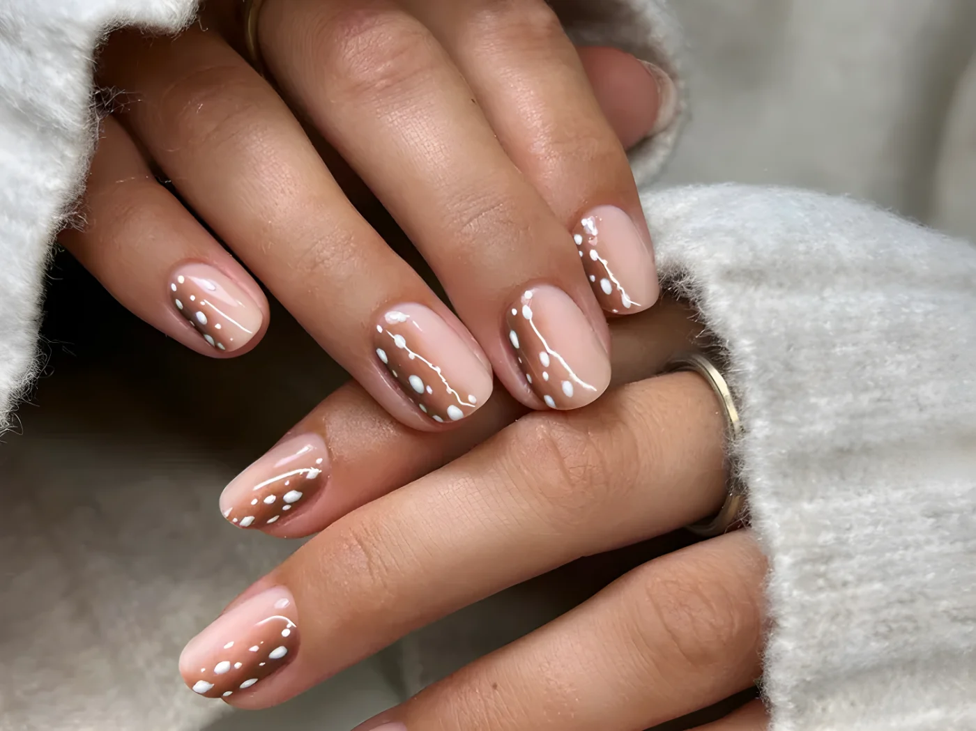 Short fawn nails against cream sweater sleeves