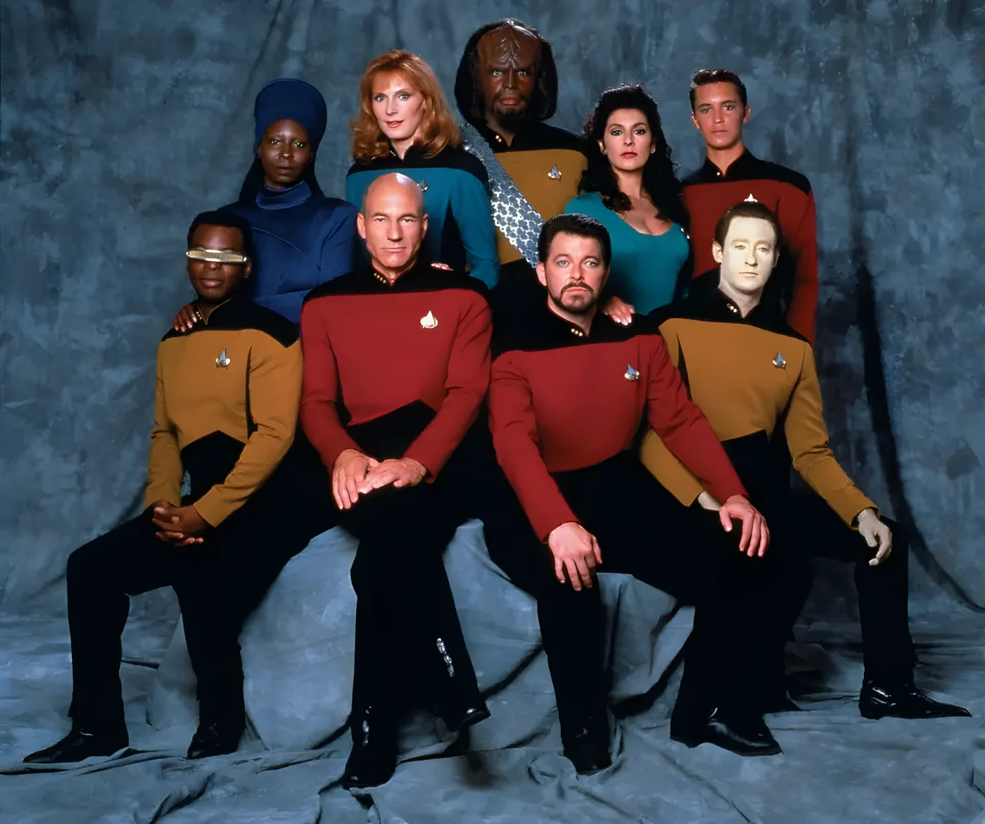 Star Trek: The Next Generation cast in 1987. Pictured are from left, front row, American actor LeVar Burton (as Lieutenant Commander Geordi La Forge), British actor Patrick Stewart (as Captain Jean-Luc Picard), and American actors Jonathan Frakes (as Commander William T. Riker) and Brent Spiner (as Lieutenant Commander Data); from left, back row, American actors Whoopi Goldberg (as Guinan), Gates McFadden (as Doctor Beverly Crusher), and Michael Dorn (as Lieutenant Worf), British-American actress Marina Sirtis (as Counselor Deanna Troi), and American actor Wil Wheaton (as Wesley Crusher).