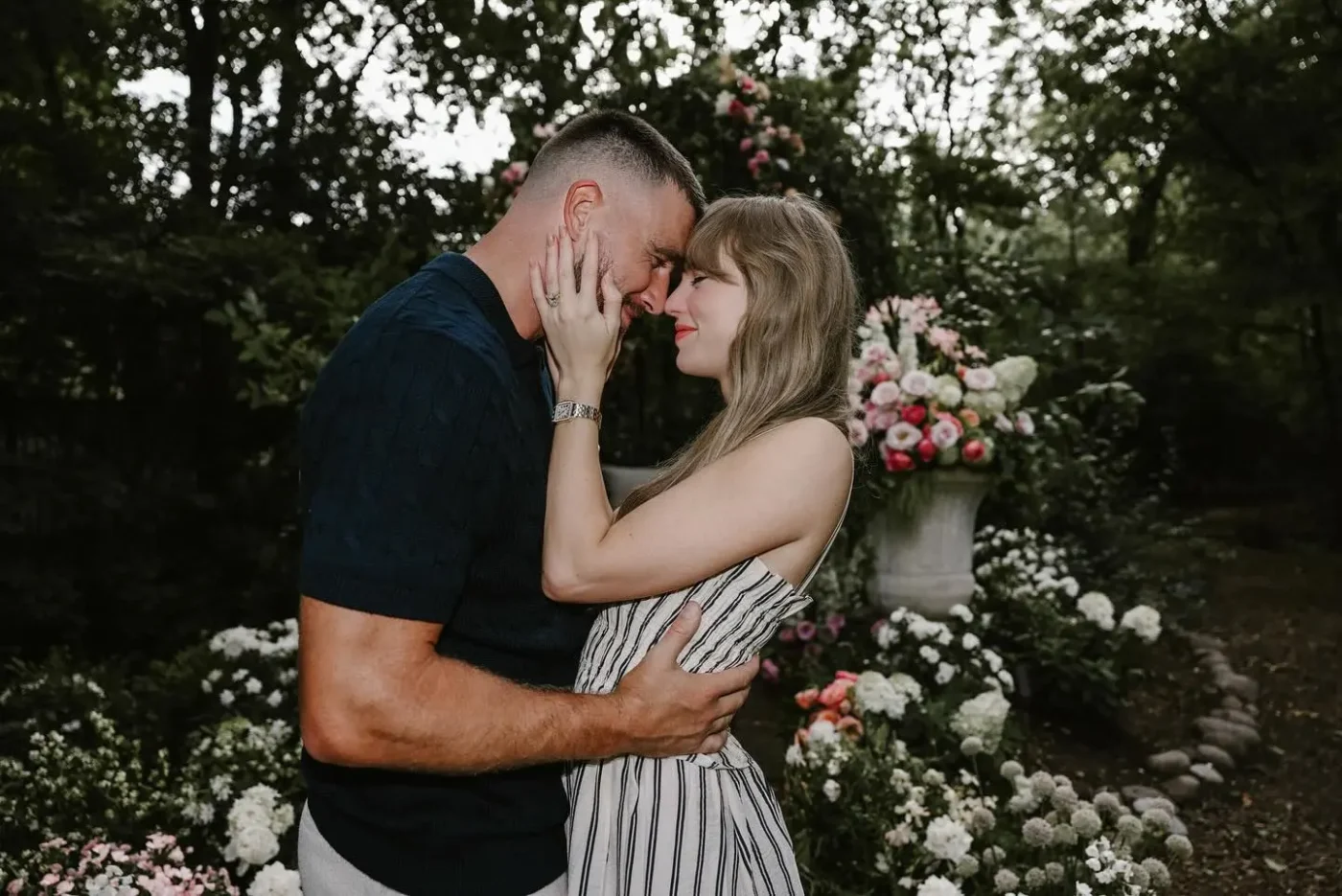 Taylor Swift and Travis Kelce embrace in a garden.