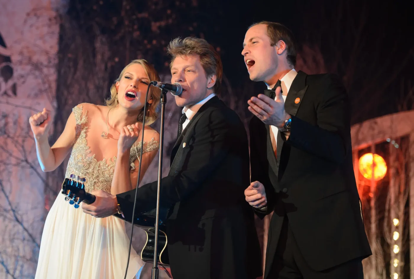 Taylor Swift, Jon Bon Jovi, and Prince William singing on stage into a microphone.