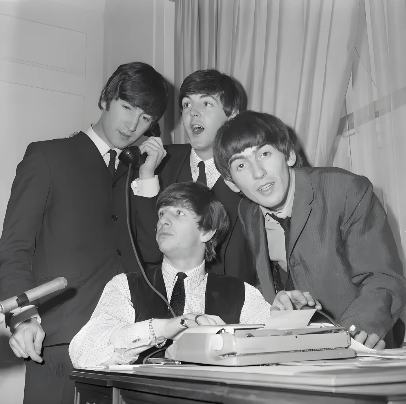 The Beatles, Great Britain's gyrating song sensation, gather around phone in their Hotel Plaza suite after arriving in New york Feb. 7. Airport officials say thousands of teenage youths were on hand to greet the singers and accorded them the greatest reception ever rendered a theatrical prsonality. Seated at phone is Ringo Starr. Standing, left to right are: George Harrison, john Lennon and PAul McCartney, 1964
