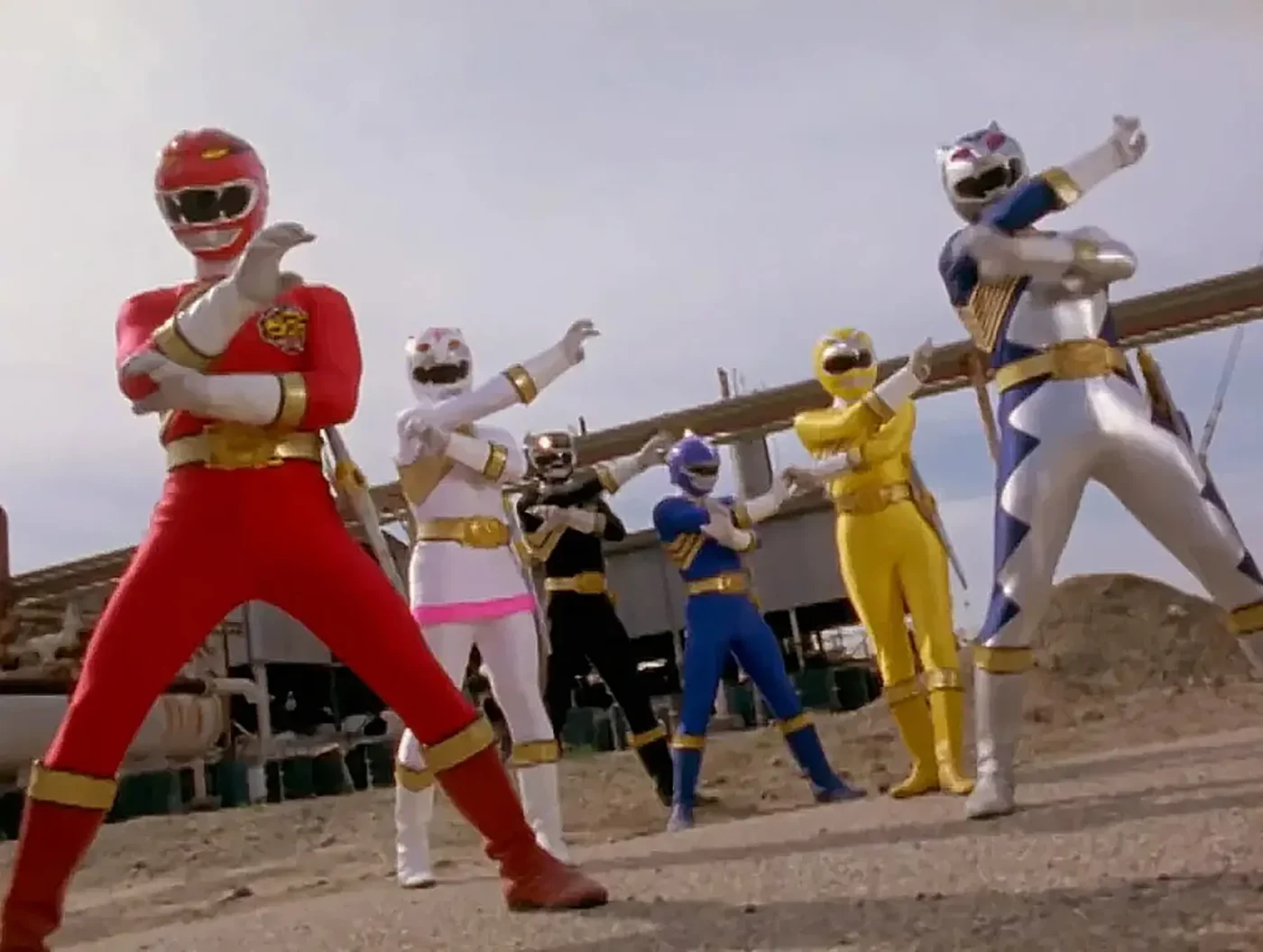 The six Power Rangers Wild Force members strike a pose outdoors in an industrial area.