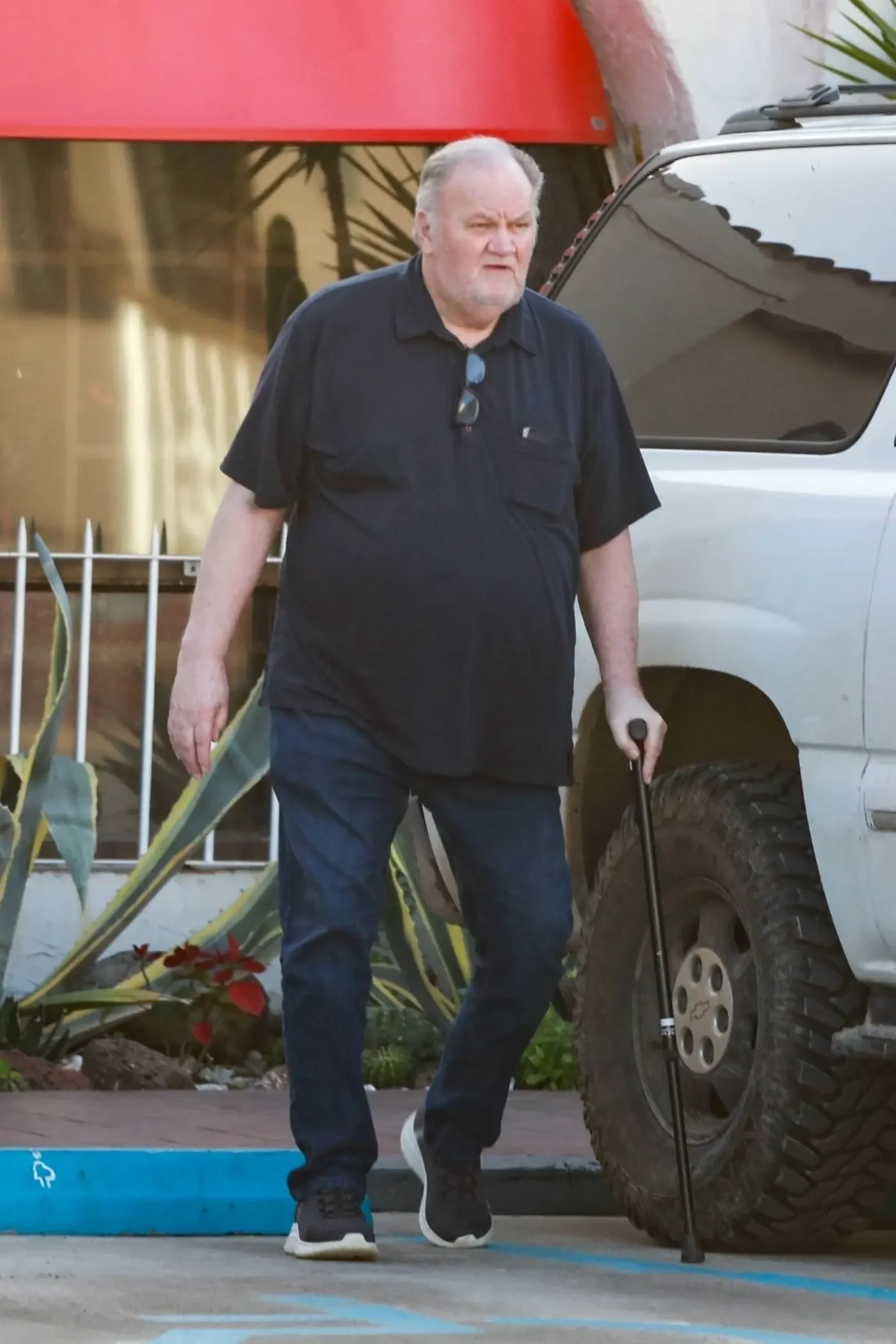 Thomas Markle walking outside with a cane next to a white SUV.