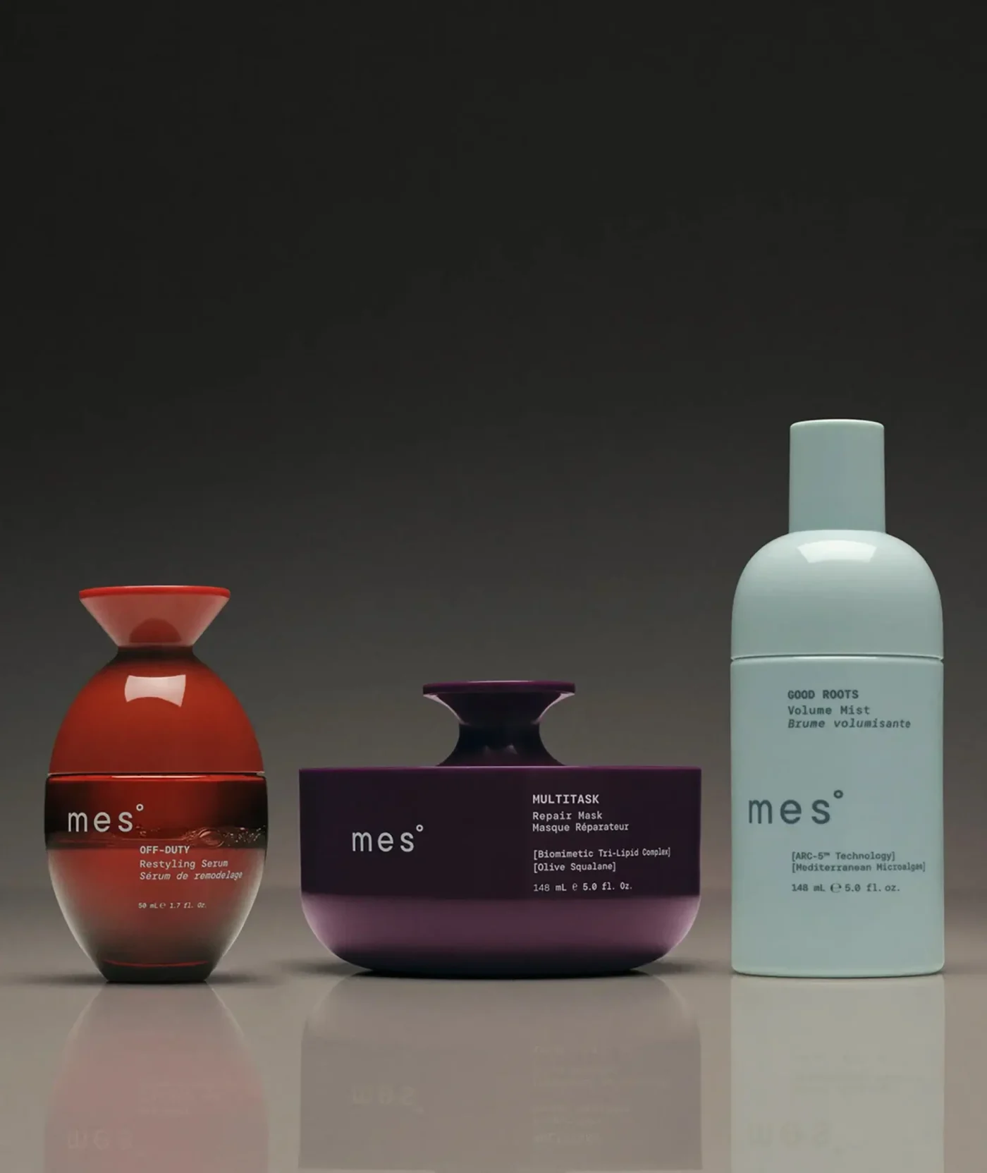 Three Mes hair care products, including Off-Duty Restyling Serum in an orange bottle, Multitask Repair Mask in a purple jar, and Good Roots Volume Mist in a light blue bottle, arranged in a row.