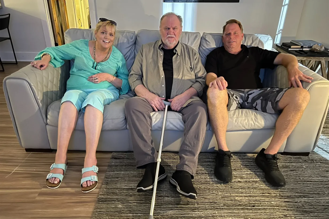 Three people sit together on a light grey couch.