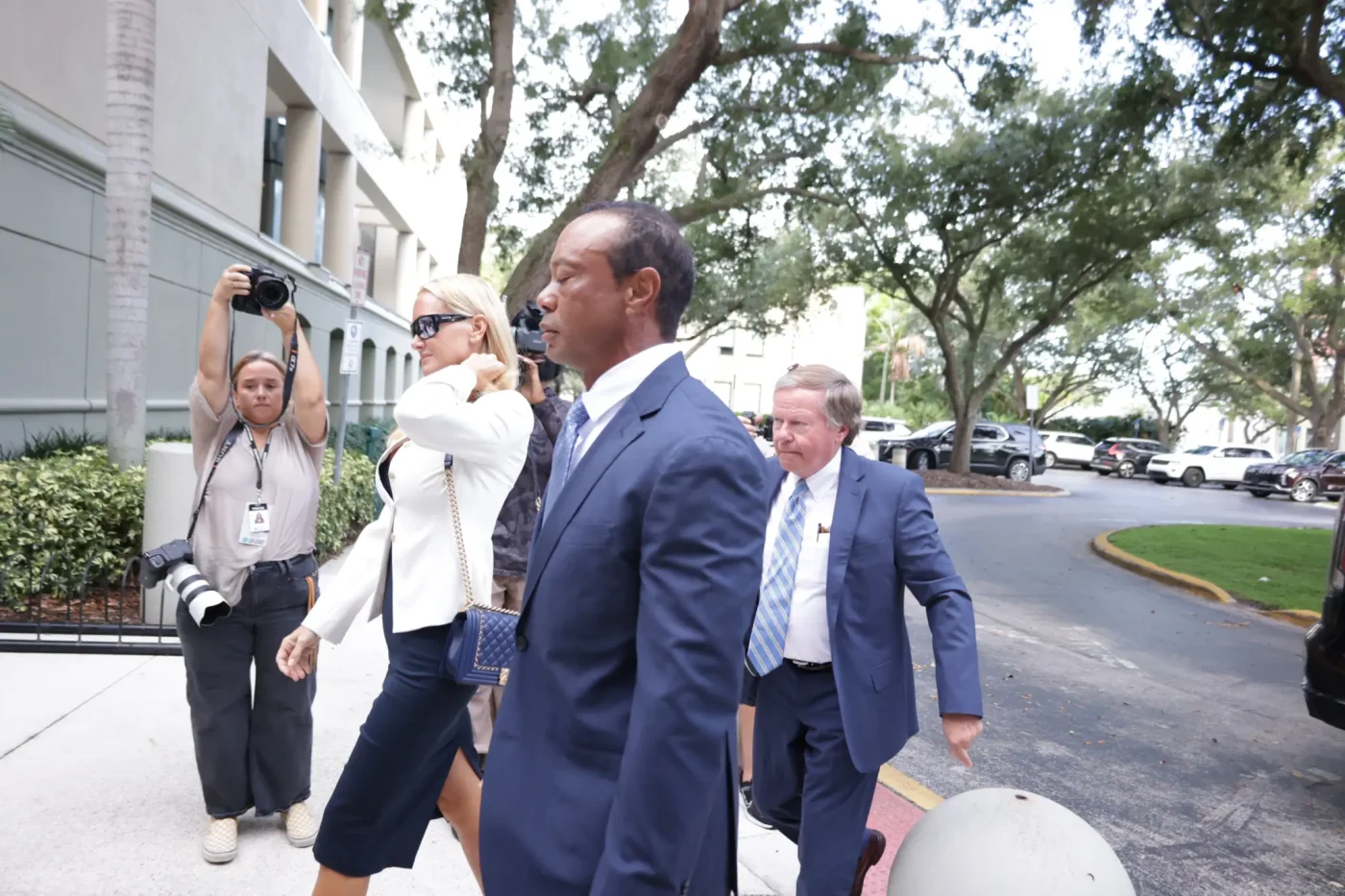 Tiger Woods and Vanessa Trump walking together near a building, surrounded by people and cameras.