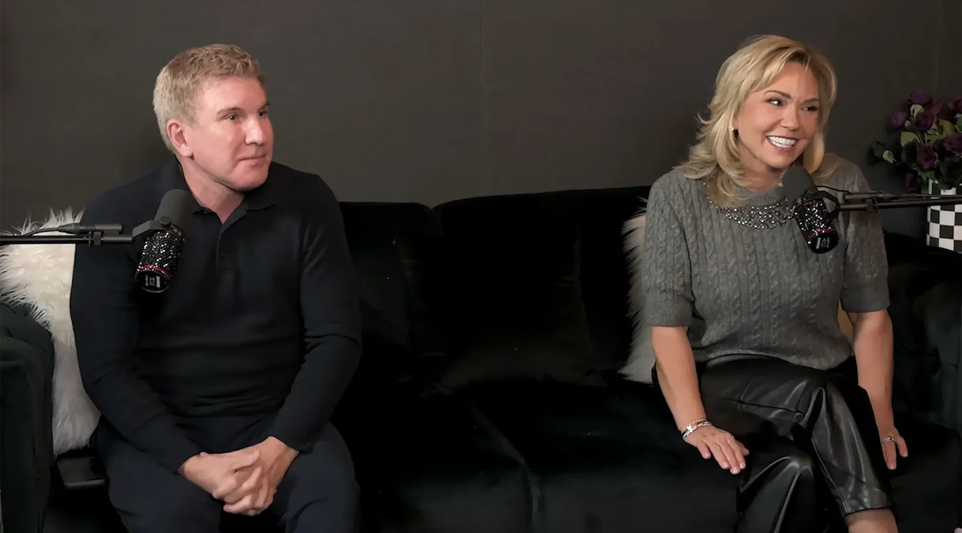 Todd and Julie Chrisley seated on a black couch in front of microphones.