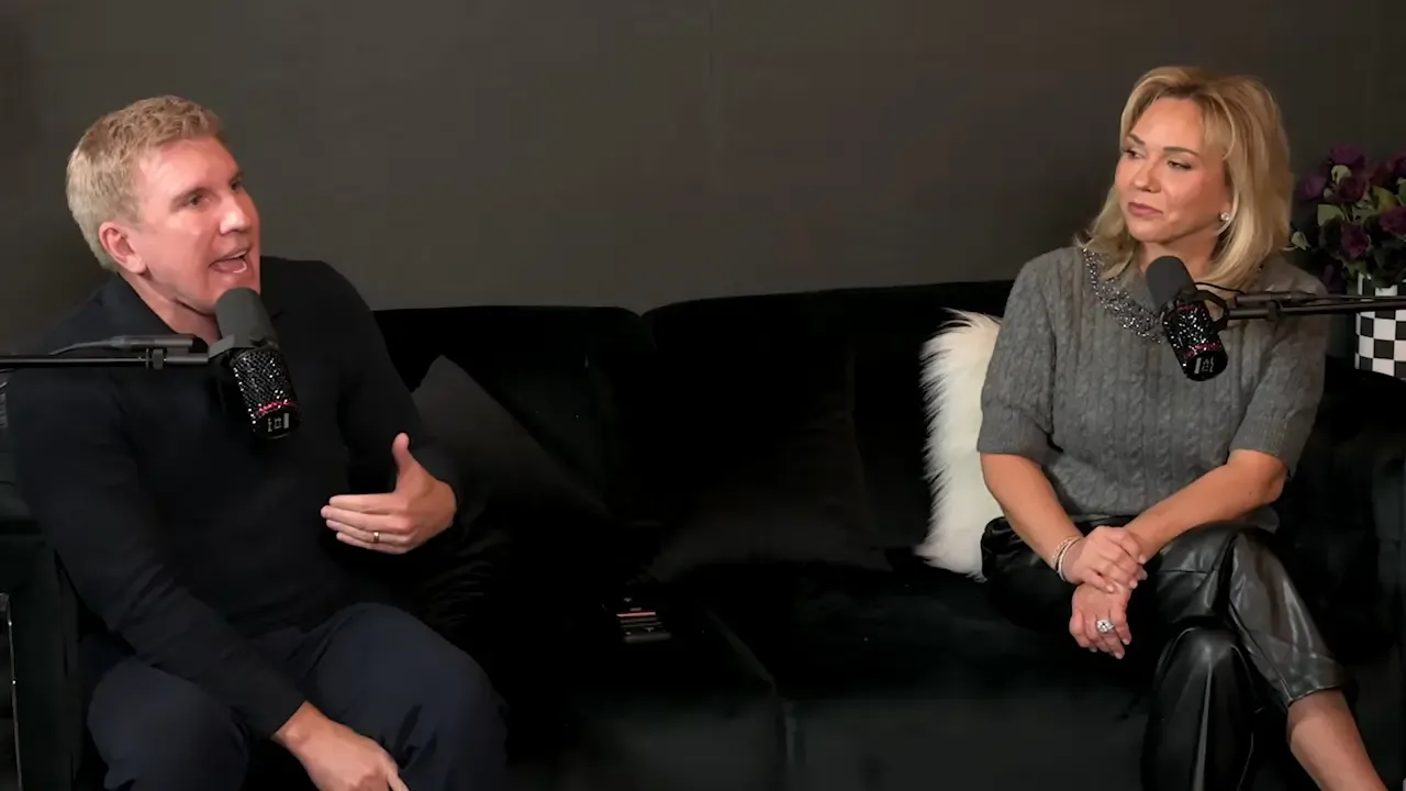 Todd Chrisley talking and gesturing while seated on a black sofa next to a woman speaking into a microphone.