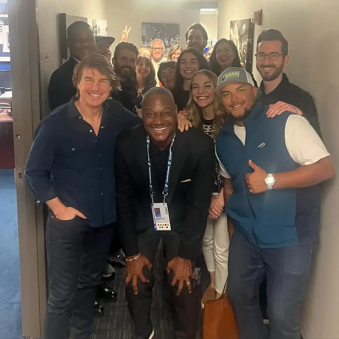 Tom Cruise and Connor Cruise posing with Derrick Brooks and a group of people in a hallway.