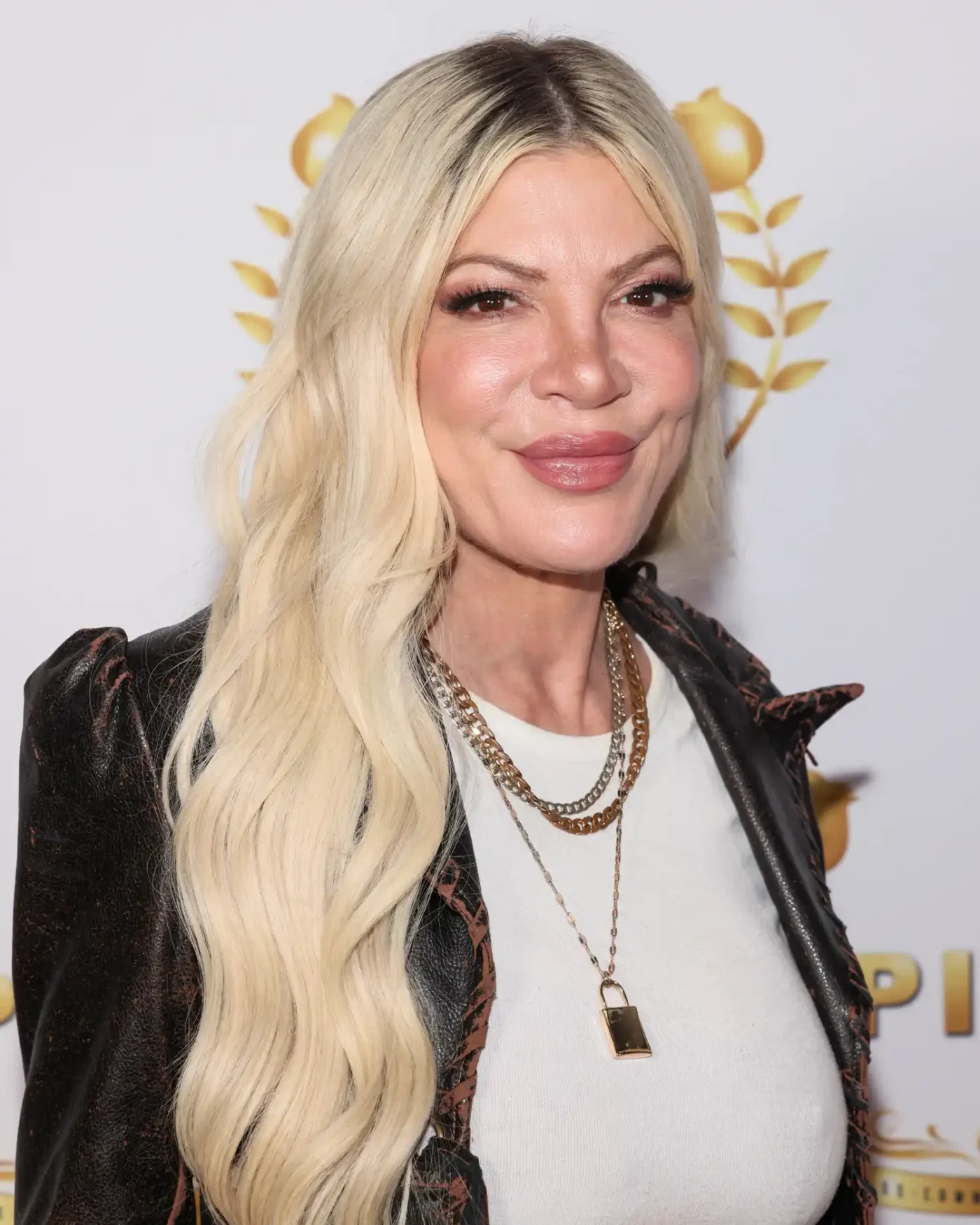 Tori Spelling in a leather jacket smiling at an event in 2025