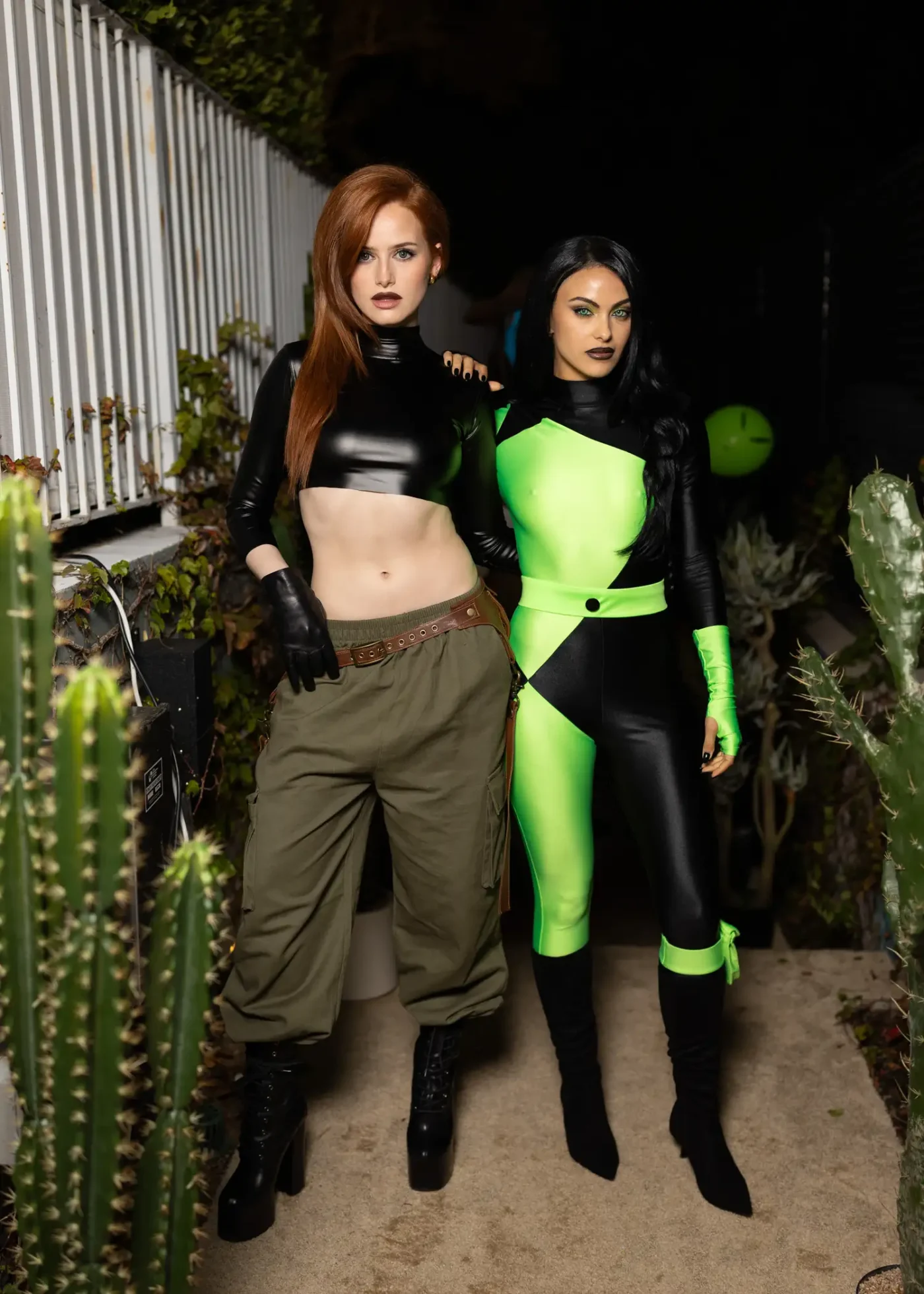Two people in costume posing together outdoors one in a black crop top and cargo pants the other in a black and green superherothemed outfit