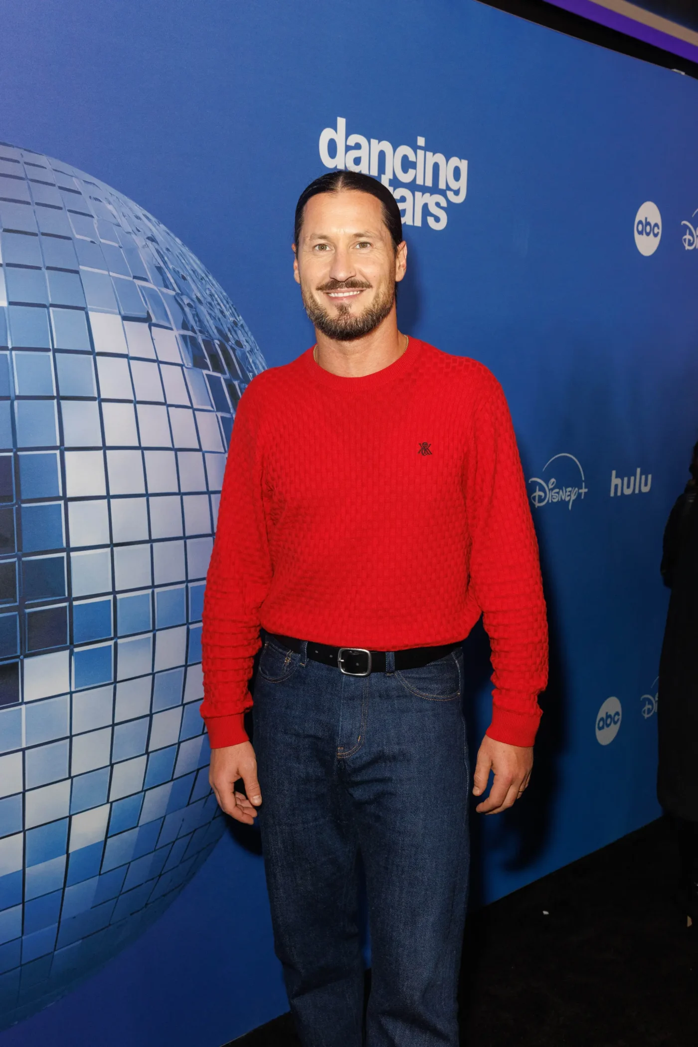 Val Chmerkovskiy attends the Dancing with the Stars press line, wearing a red sweater and jeans.