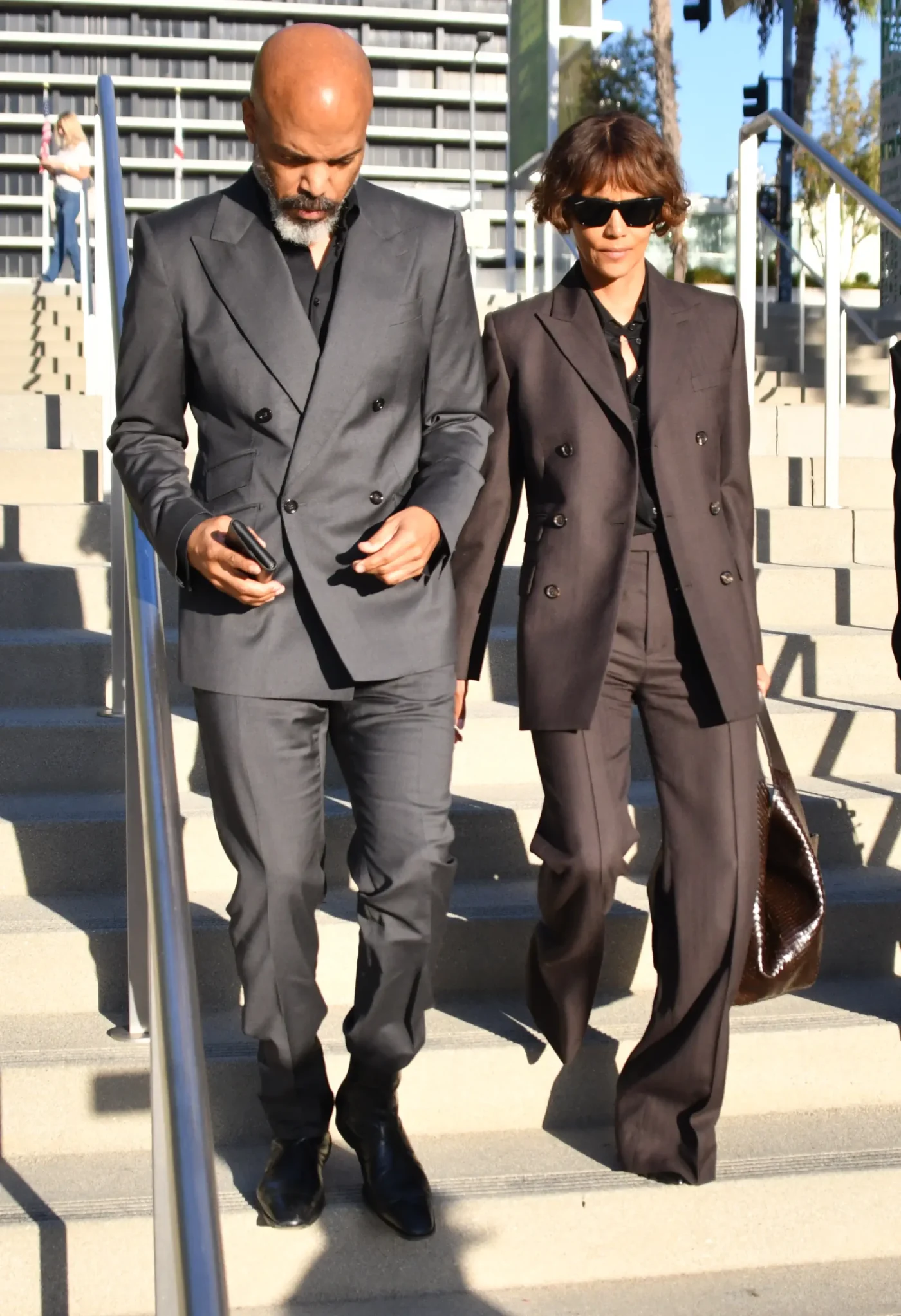 Van Hunt and Halle Berry walk down outdoor stairs together, both wearing tailored business suits.