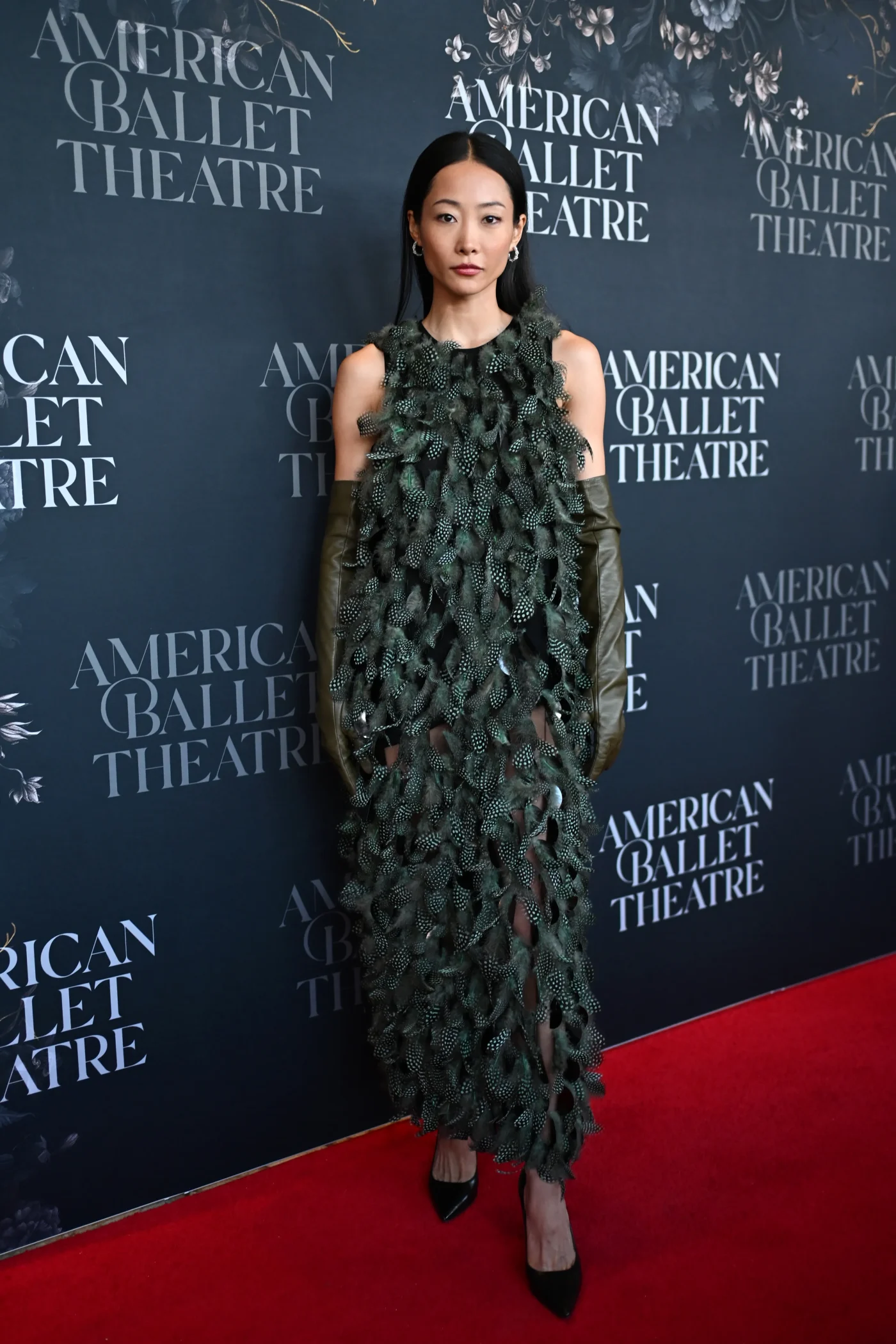WanTing Zhao poses on the red carpet at the American Ballet Theatre Fall Gala, wearing a sleeveless feather-covered dress paired with dark green leather gloves.