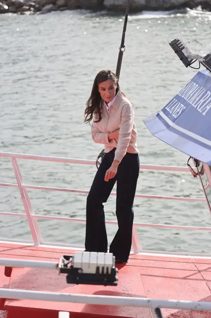 Woman with long hair in a pink sweater and dark pants standing on a boat.